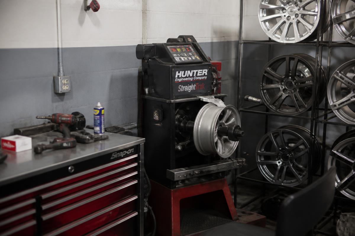 Alloy rims on a shop rack beside a wheel straightening machine and tools